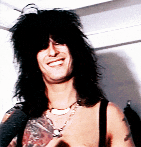 a man with long black hair and a necklace smiles