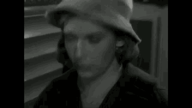 a black and white photo of a woman wearing a hat covering her mouth .