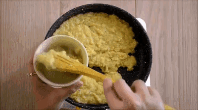 a person is pouring a yellow liquid into a pan with a yellow spoon .