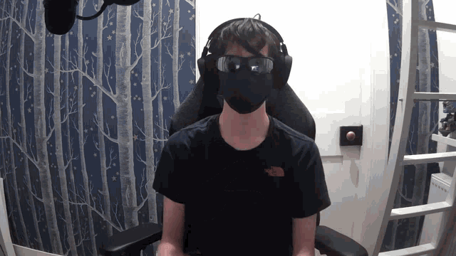 a man wearing a mask and headphones is sitting in a chair in front of a microphone