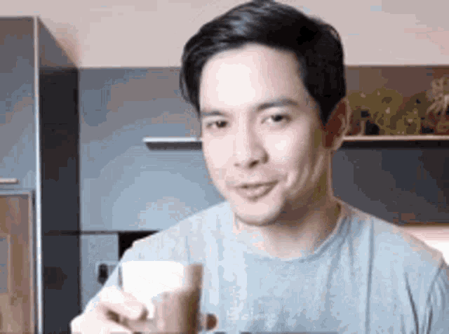 a man in a gray shirt is drinking a cup of coffee .