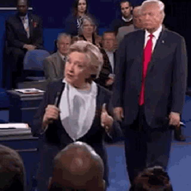 a man in a suit and tie is standing next to a woman holding a microphone in front of a crowd .