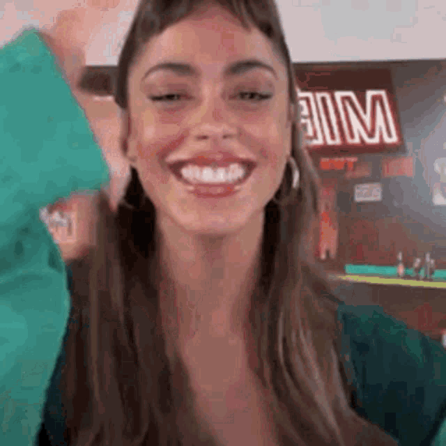 a woman is smiling and looking at the camera while wearing a green shirt and earrings .