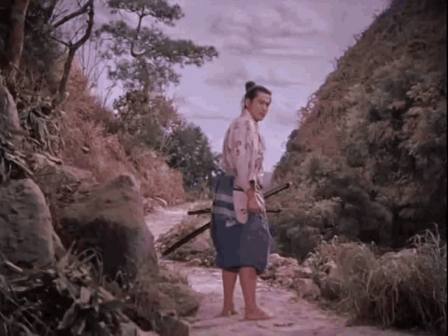 a man in a kimono is holding two swords on a dirt path