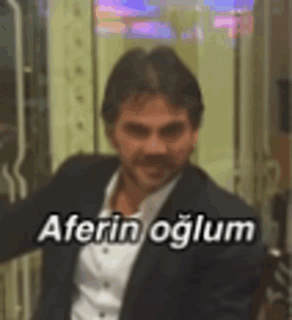 a man in a suit and white shirt is standing in front of a sign that says ' aferin oglum ' on it .