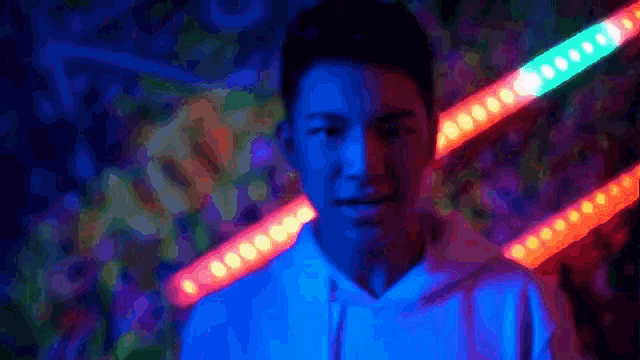 a man in a white hoodie is standing in front of a wall with neon lights on it .