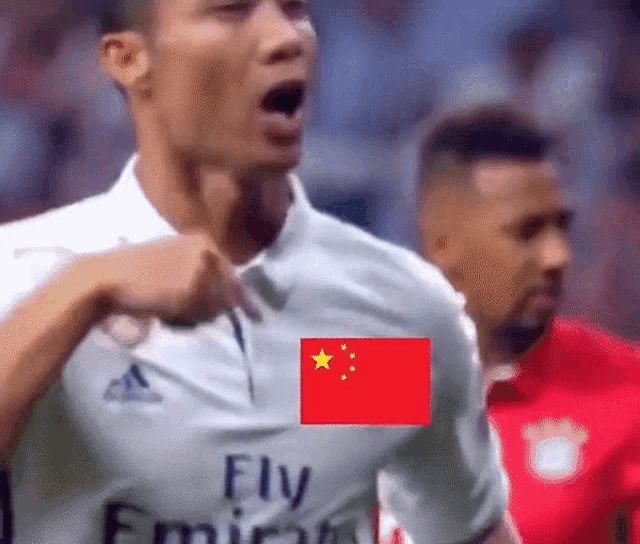 a soccer player wearing a fly emirates jersey is pointing at a flag
