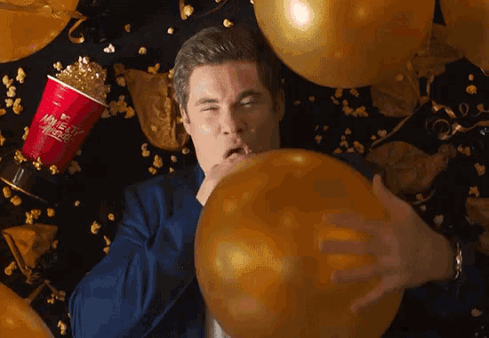 a man blowing up a gold balloon in front of a movie ticket