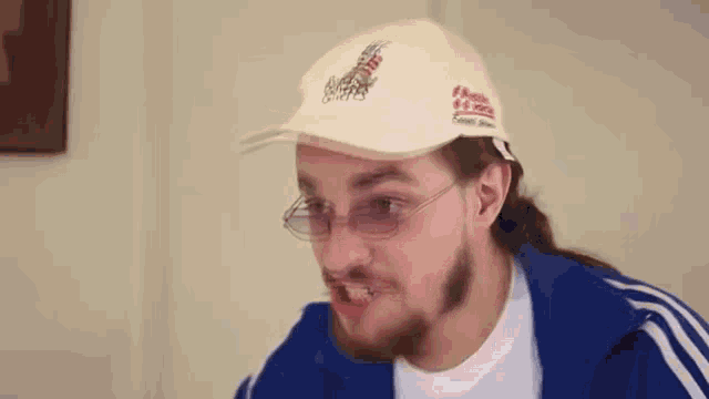 a man with a beard is wearing a white hat and glasses .