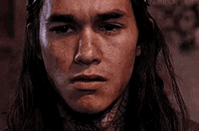 a close up of a man 's face with long hair and a bloody face .