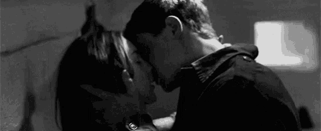 a black and white photo of a man and a woman kissing .