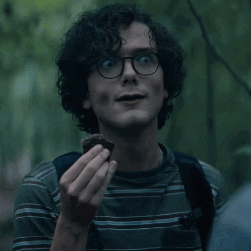 a man with curly hair and glasses is holding a piece of food