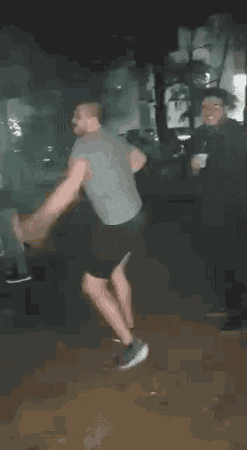 a man in a grey shirt and black shorts is dancing on the ground