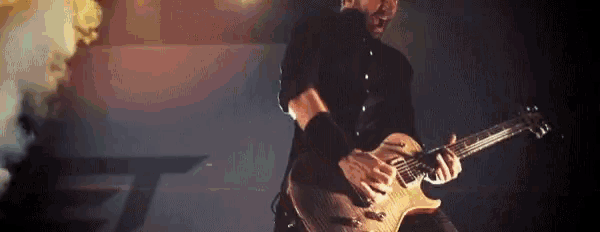a man in a black shirt is playing a guitar in front of smoke