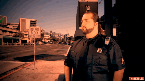 a man in a police uniform stands in front of a do not block intersection sign