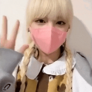 a blonde girl wearing a pink mask and braids is giving a peace sign .