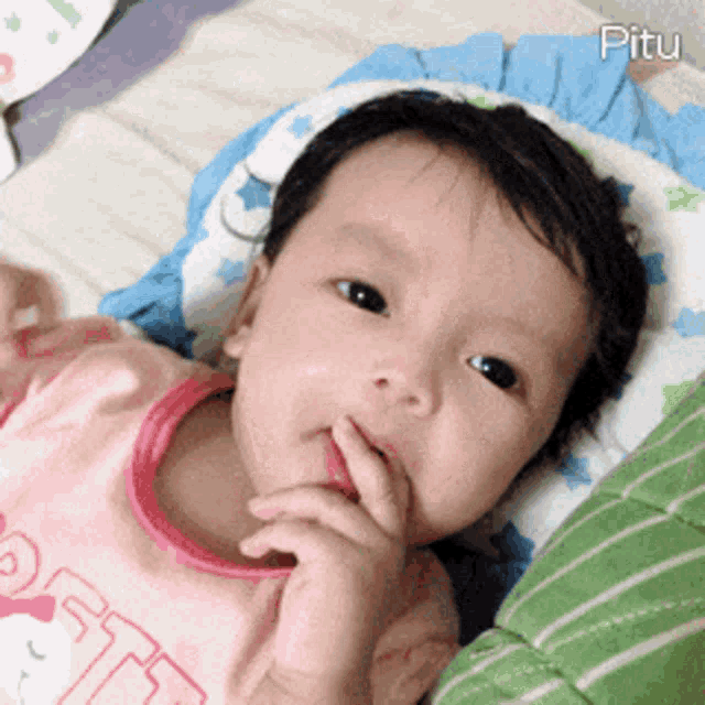 a baby is laying on a bed with a pillow that says pitu on it