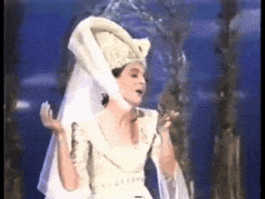 a woman in a white dress and veil is singing a song