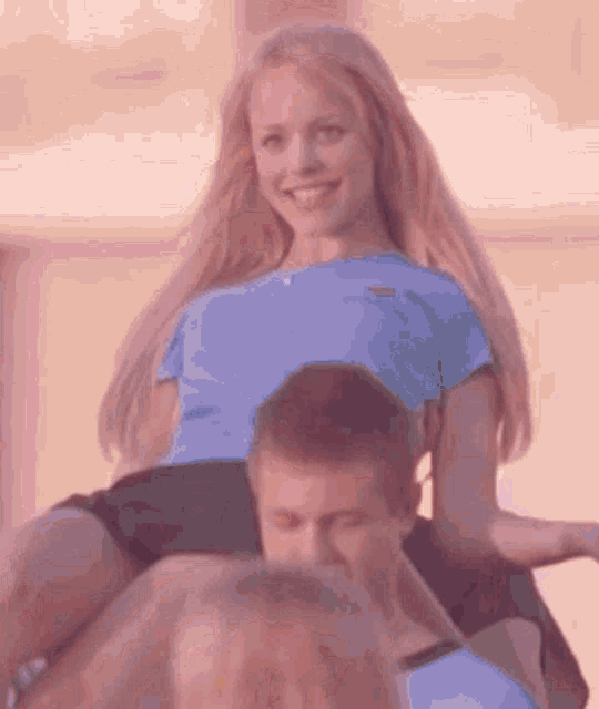 a woman in a blue shirt is sitting on a man 's shoulders and smiling .