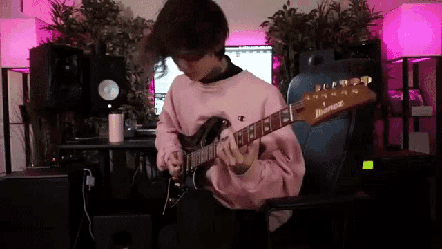 a man in a pink sweatshirt is playing an electric guitar in a room .