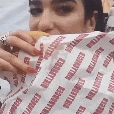 a woman is eating a hamburger wrapped in a paper that says billabong .
