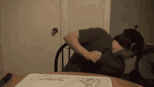 a man is sitting at a table writing on a piece of paper with a pen