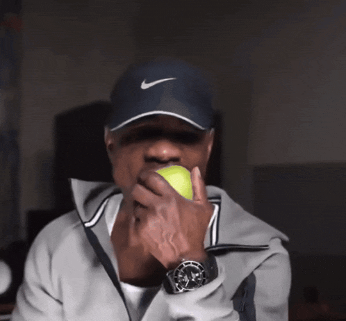 a man wearing a nike hat holds a tennis ball in his hand