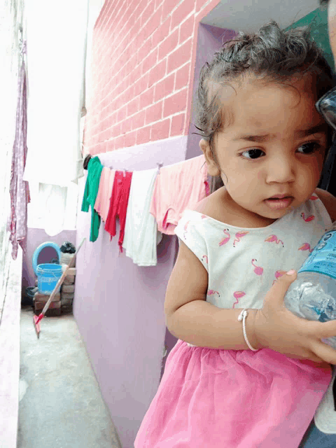 a little girl wearing a pink flamingo dress holds a bottle of water