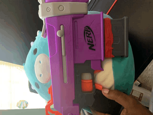 a purple nerf gun is laying on a blue stuffed animal