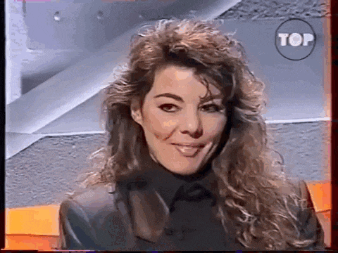 a woman with long curly hair is smiling and looking at the camera while wearing a black jacket .