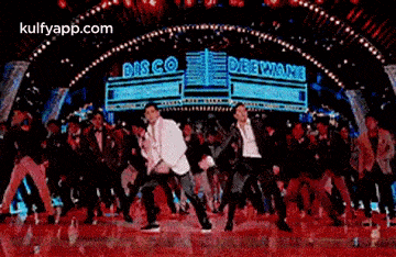 a group of people are dancing on a stage in front of a neon sign that says disco .