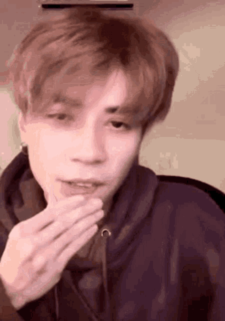 a young man in a purple hoodie is blowing a kiss while sitting in front of an air conditioner .