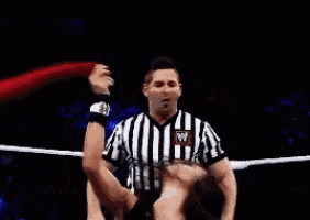 a woman in a wrestling ring with a referee standing behind her .