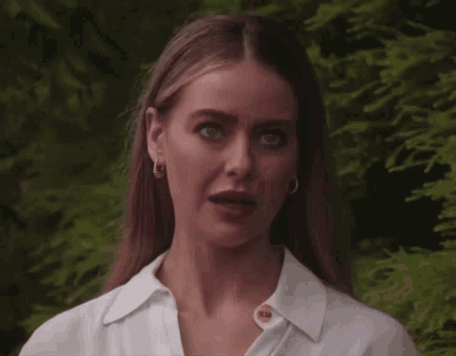 a woman wearing a white shirt and hoop earrings looks sad