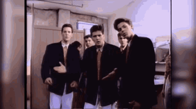 a group of men in suits and ties are dancing in a room .