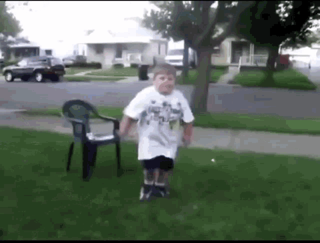 a boy in a white shirt is jumping in the air in front of a green chair .