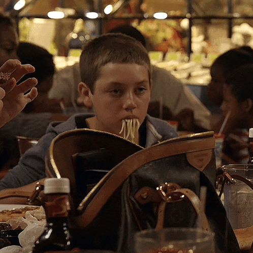 a young boy is eating noodles from a louis vuitton bag
