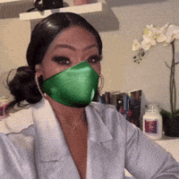 a woman wearing a green face mask is sitting at a desk .