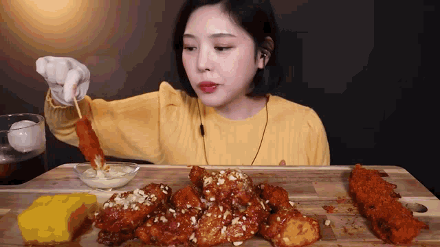 a woman in a yellow shirt is eating fried chicken on a cutting board