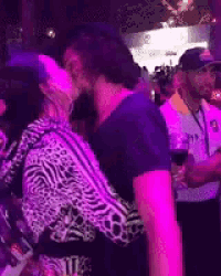 a man and woman are kissing in a crowded room with purple lights