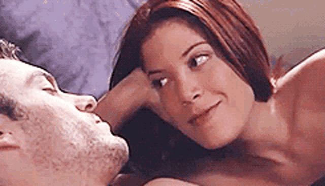 a man and a woman are laying on a bed and the woman is touching the man 's face