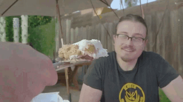 a man wearing a shirt that says loud is eating a cake