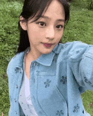 a woman wearing a blue denim jacket with flowers on it takes a selfie