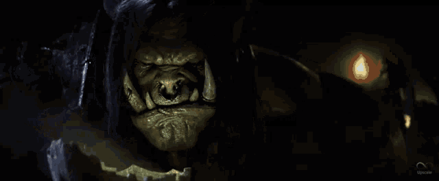 a close up of a monster 's face in a dark room with a fire in the background