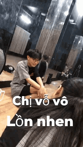 a man and a woman are sitting on the floor in front of a mirror with the words chi vo vo lon nhen below them