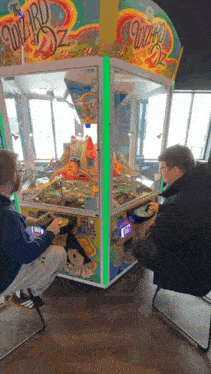 two men playing the wizard of oz claw machine