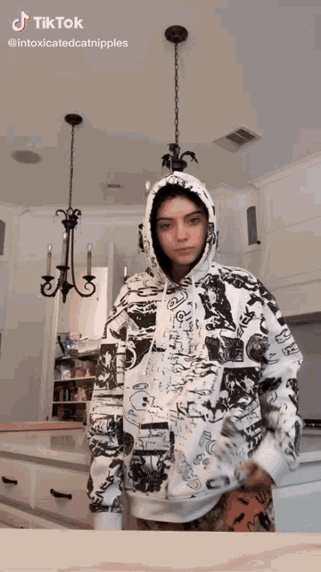 a girl in a hoodie is standing in a kitchen