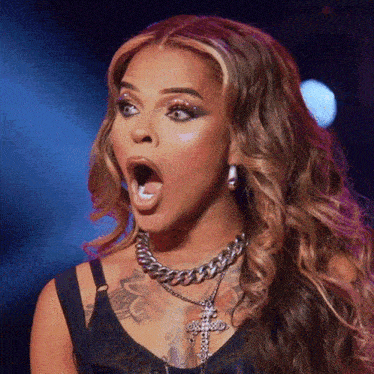 a woman with a surprised look on her face is wearing a necklace with a cross on it