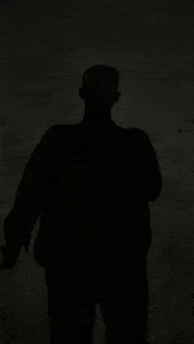 a shadow of a man is standing in the dark .