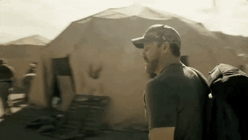 a man wearing a hat and a backpack is standing in front of a tent .